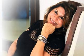 Smriti wearing a black dress relaxing on a chair and looking at the camera as she talks about her abdominal cancer