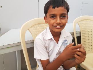 A young boy in a white shirt sitting on a cream coloured plastic chair 