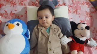 A child lying in bed with soft toys on either side of him