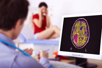 Image: A woman holding her head in the background and a doctor looking at a brain scan showing brain tumour