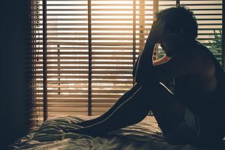 Image: Stock pic of a man sitting depressed, holding his head, next to a window