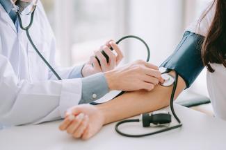 Stock pic of a doctor in a white coat measuring the BP of a patient whose arm has a BP monitor band