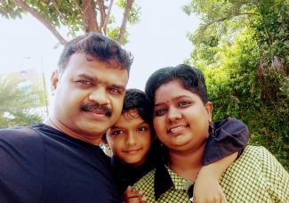 Image of Pavithra, a brain tumor survivor in a green dress with her husband in black and son