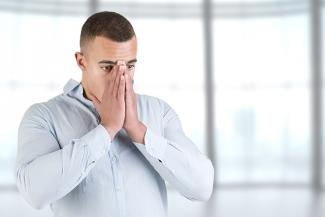 A man in front of windows holding his face while having a panic attack