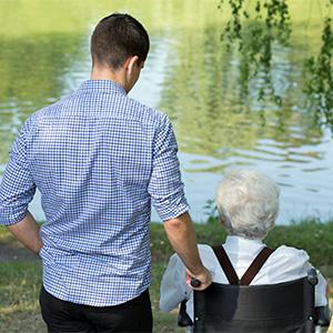 An elderly person on a wheelchair looking out to the lake with a male caregiver standing next to him