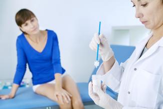 A woman in blue top sitting on an examination table while the doctor in a white coat looks at results of a test