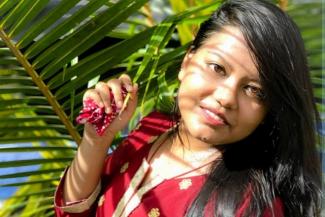 A young woman in a red dress standing next to a palm frond