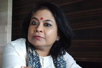 Image Description: A dark haired Indian lady with a bindi wearing a white dress and a printed scarf or dupatta draped over her shoulders