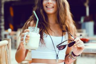 Image: A young lady in a summery white crop top, a cool drink with a straw in hand, dark glasses in the other hand