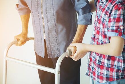 Image Description: An elderly person with a walker and supported by a caregiver