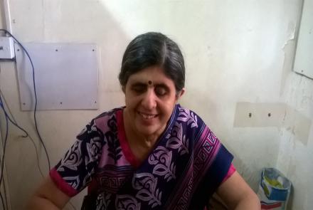 Dipti Bhatia, visually impaired from birth wearing a blue red and pink kurta and dupatta at her desk with wires  visible in the background