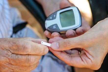 A pair of hands, one holding a glucometer and the other a pill showing support of a caregiver to a diabetic patient