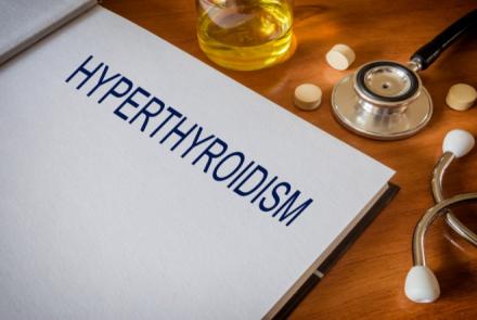 Stock pic of a writing pad with the heading Hyperthyroidism and stethoscope and pills on a wooden table top