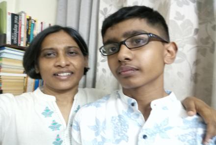 A mother and her autistic son both wearing white and standing against a book shelf