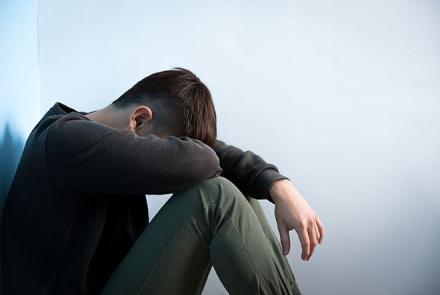 Man in a black long sleeved shirt and khaki pants bending down demonstrating depression