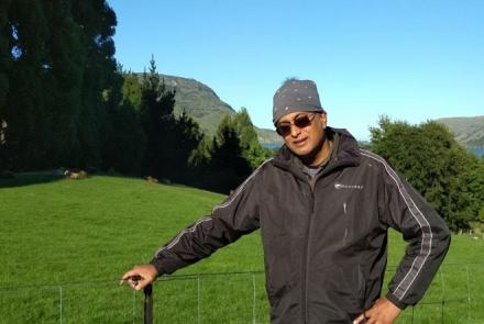 Image: A man facing the camera in a green outdoor setting, wearing sunglasses, travelling after Deep Brain Stimulation surgery