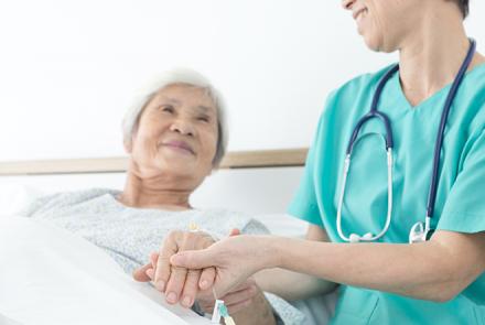 A woman in bed being tended to by a person in green scrubs with a stethoscope