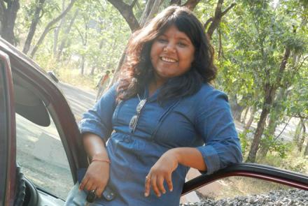 A young woman in a blue dress standing next to the open car door with a car key in her hand