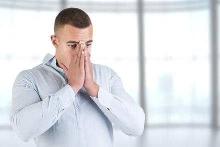 A man in front of windows holding his face while having a panic attack