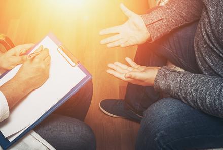 A partially visible counsellor sitting with a person with outstretched hands