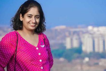 Ewing Sarcoma survivor Gauri in a pink dress in the foreground and some buildings in the background