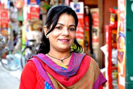 Mona Balani, a young Indian woman wearing a bright red kurta and a colourful dupatta set against a colourful market background