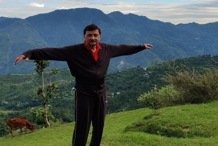 A person with Parkinsons standing on top of the mountains with his arms outstretched 