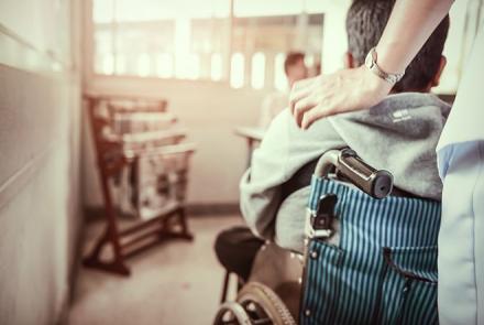 Image description: Partial picture of a person on a wheelchair being pushed by a carehver