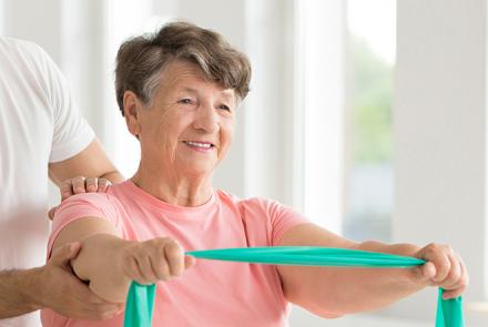 A woman in a pink t shirt stretching a green resistance band