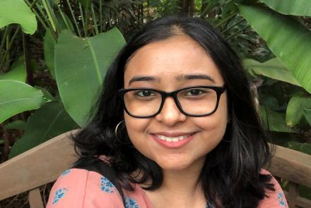 Young woman with specs in front of a leafy plant