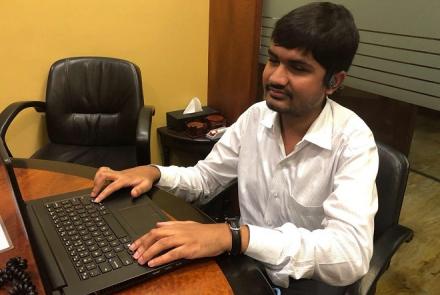  A visually impaired young man in a white shirt working on his computer at a desk in an office